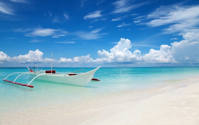 A white boat floats in turquoise water near a sandy beach under a blue sky.