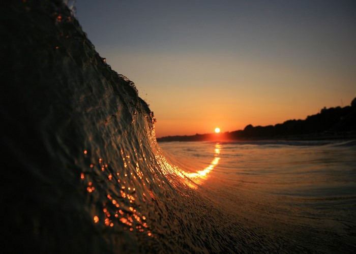 Wave crashing at sunset with sun reflection on water