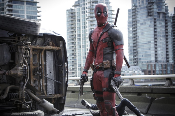 Deadpool with guns next to overturned car