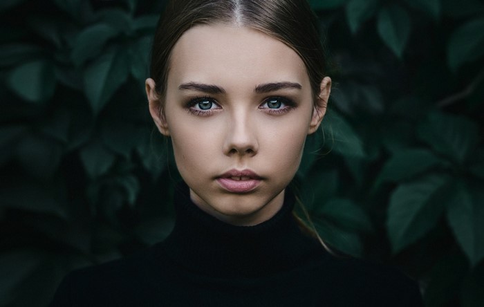 Woman in black turtleneck with dark green leaves background