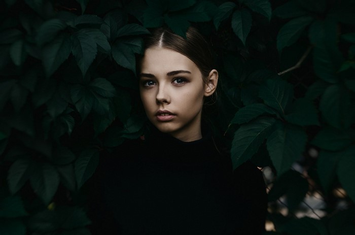 Woman in black shirt surrounded by dark green leaves