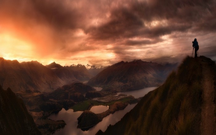 Photographer on mountain peak overlooking lake at sunset