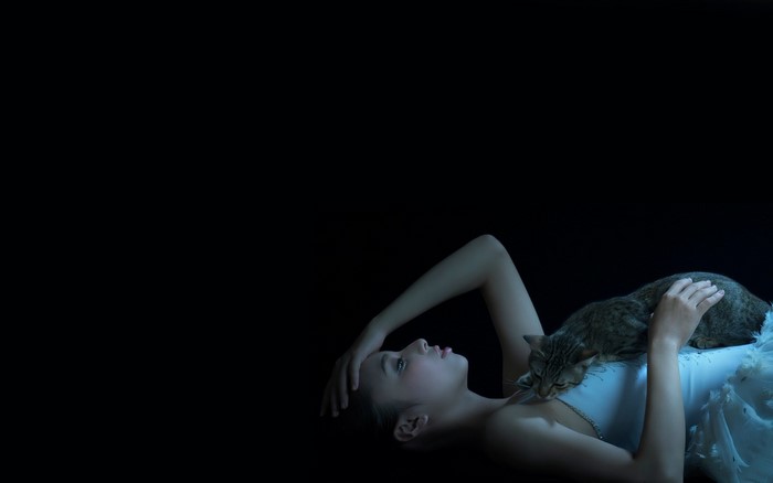Woman with cat lying down in darkness