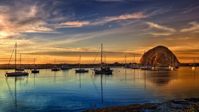 Sailboats in a harbor at sunset with Morro Rock