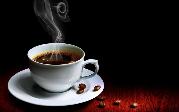 Steaming cup of coffee with coffee beans