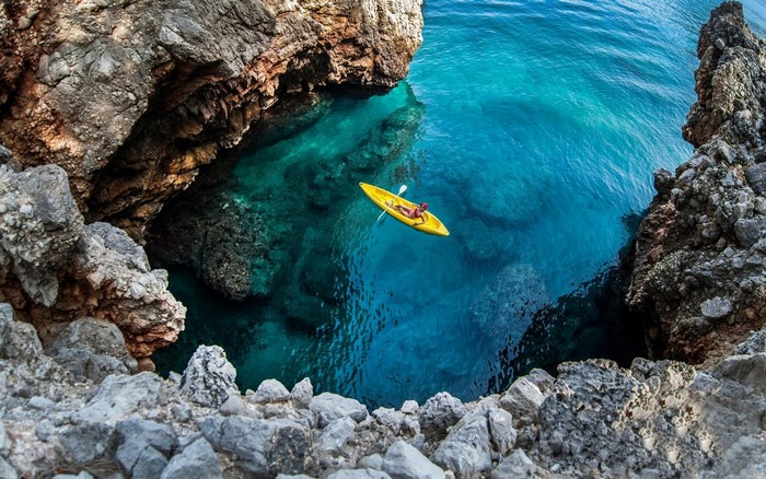 Person kayaking in a turquoise sea cave surrounded by rocks