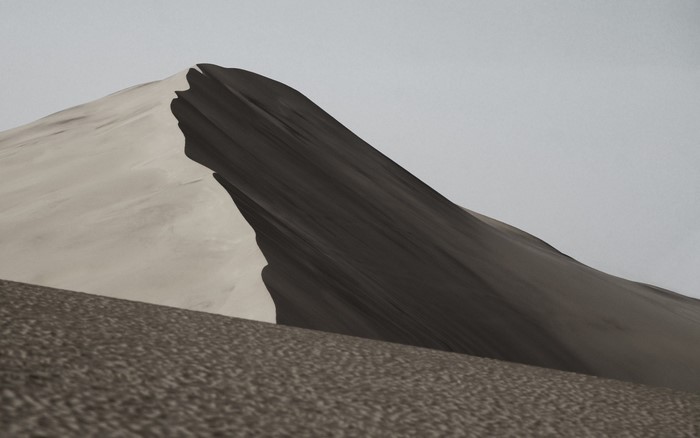 Dark and light sand dunes under a pale sky