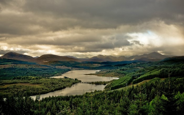 Mountain range with lake and forest under cloudy sky