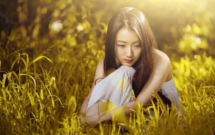 Young Woman in White Dress Sitting in Sunlit Grass