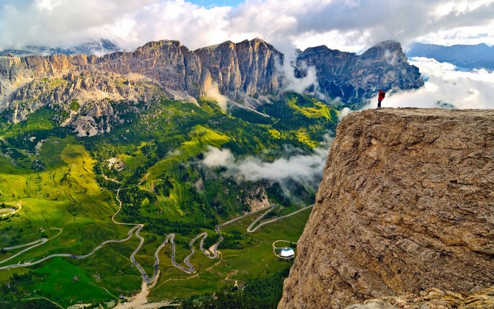 Person on cliff overlooking winding mountain road in Alps