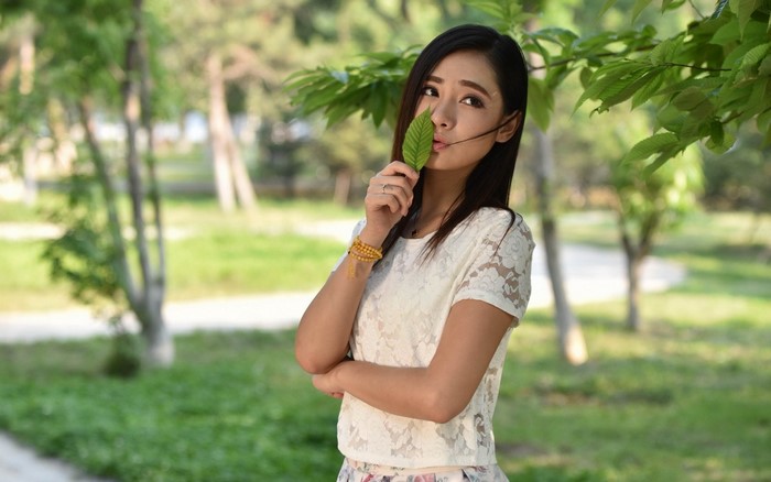 Young Asian woman holding a green leaf in a park