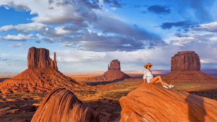 Woman in cowboy hat sitting on rock in Monument Valley