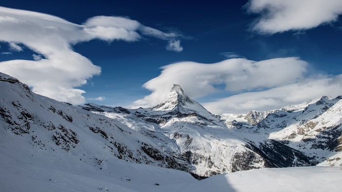 Snowy Matterhorn mountain range under a cloudy blue sky