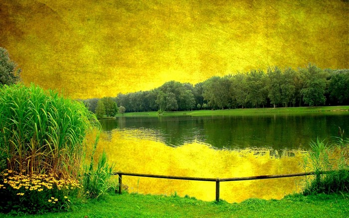 Yellow textured sky over a lake with trees and grass