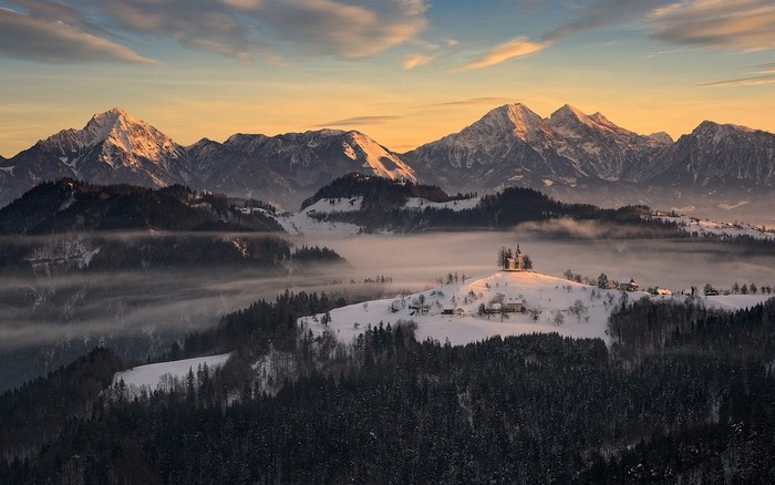 Snowy mountains with a village and church at sunrise