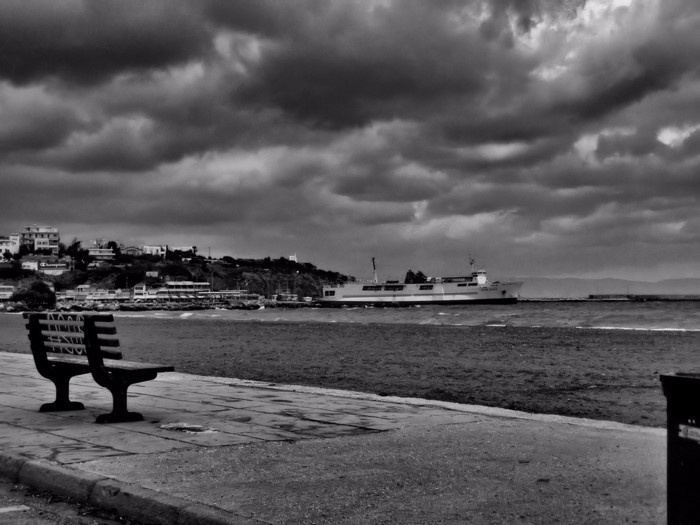 Bench overlooking sea with ship and cloudy sky in Greece