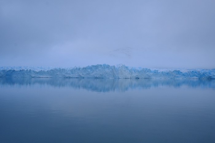 Glacier reflecting in calm water under a misty sky