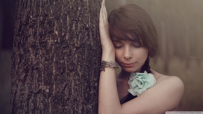 Woman leaning against a tree with a flower accessory