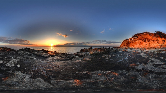 Sunset over the ocean with rocky shore and cliffside buildings