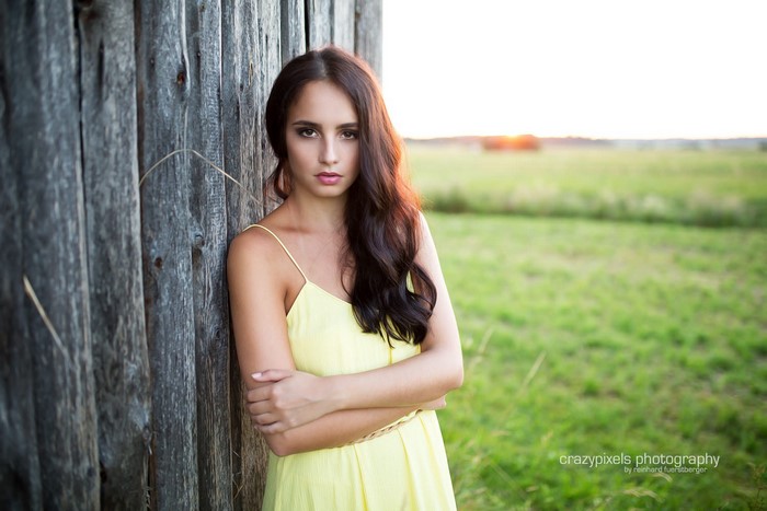 Woman in yellow dress leaning against wooden fence in field