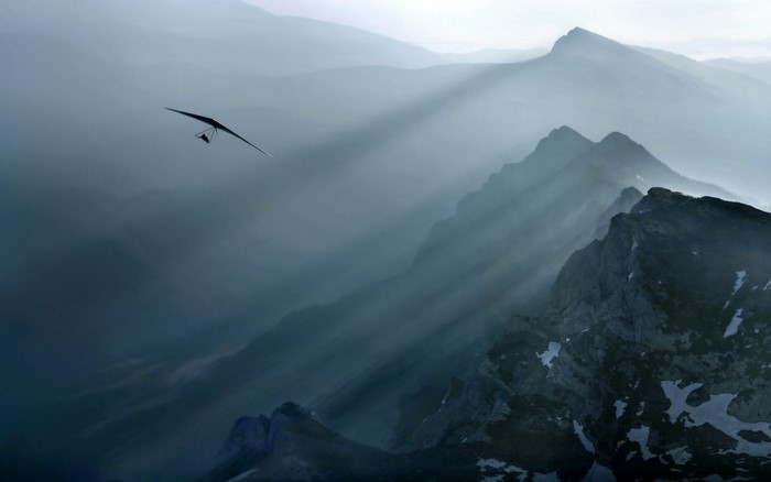 Hang glider flying over misty mountains with sun rays