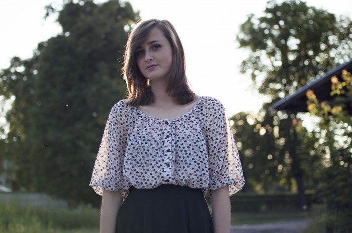 Woman in patterned blouse and black skirt outdoors