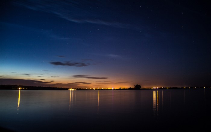 Night sky over a lake with city lights on the horizon