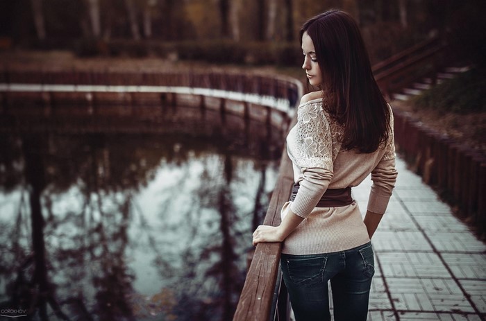 Woman in jeans and sweater on a boardwalk by a lake