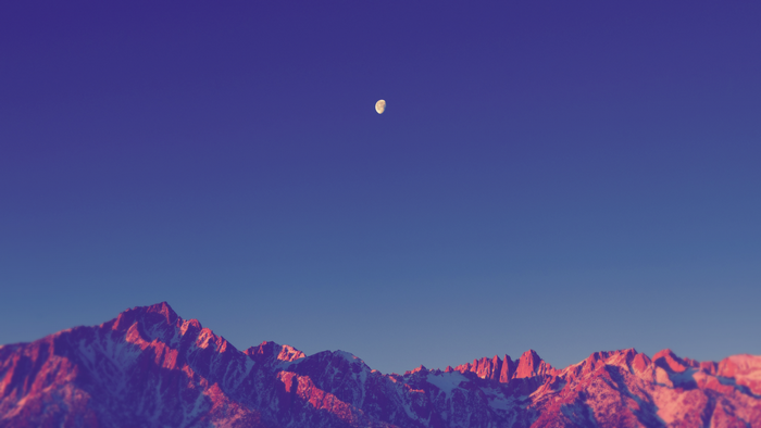 Moon over snow-capped mountains at sunset