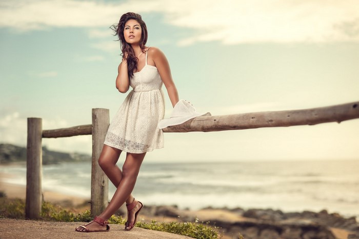 Woman in white dress leaning on a fence by the sea