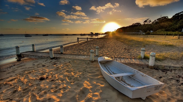 Boat on a beach at sunset with a pier