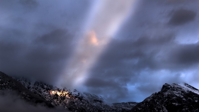 Sunlight breaking through clouds over snowy mountains
