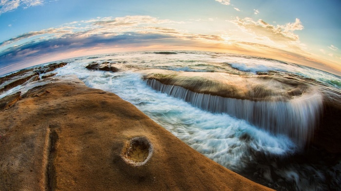 Ocean waves crashing on rocky shore at sunset