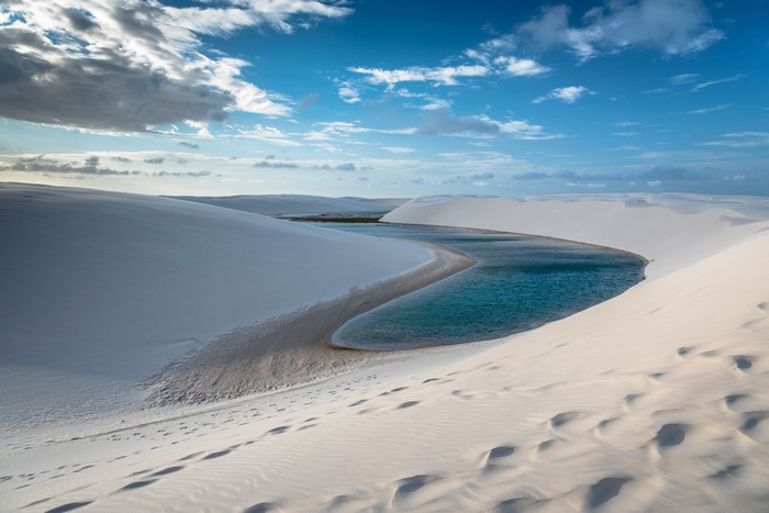 Desert dunes with a winding blue lagoon under a cloudy sky