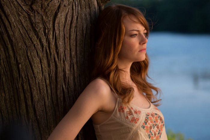 Emma Stone leaning against a tree by a lake