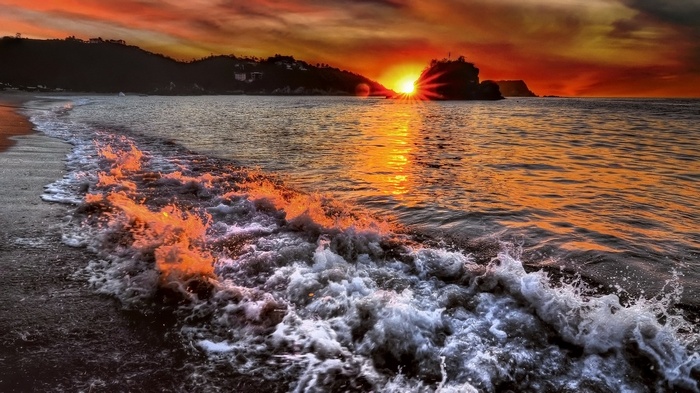 Sunset over the ocean with waves crashing on the shore