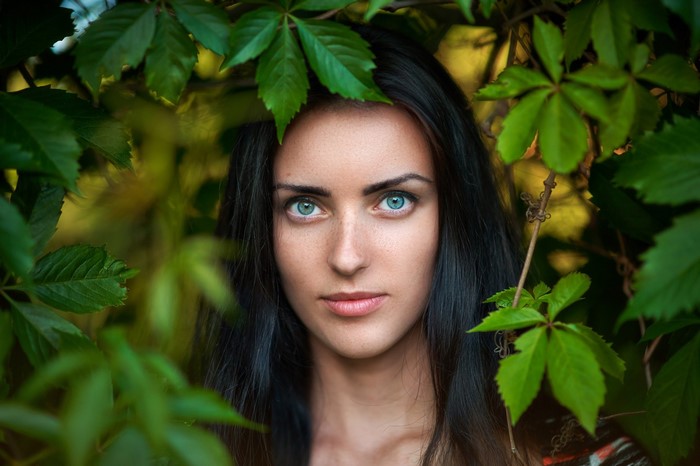 Woman with striking blue eyes surrounded by green leaves