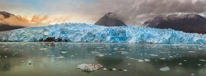 Glacier calving into the sea with mountains and clouds