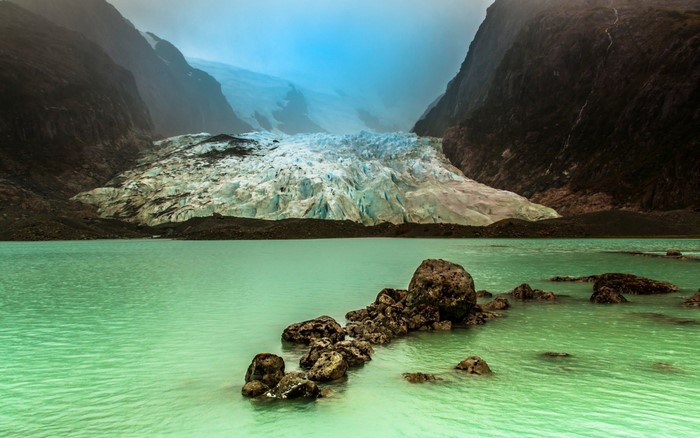 Glacier meeting a turquoise lake with rocks in the foreground