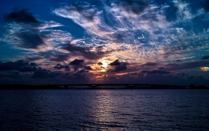 Sunset over water with a bridge and dramatic clouds