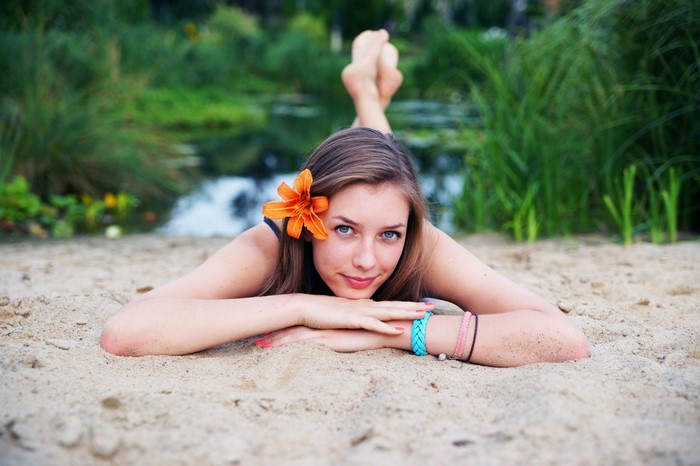 Woman with orange flower in hair lying on sand