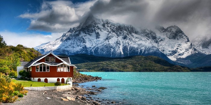 Red house by turquoise lake and snowy mountains