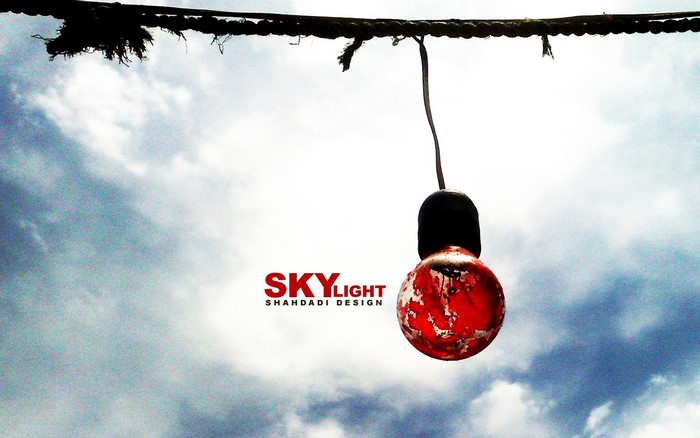 Red light bulb hanging against cloudy sky