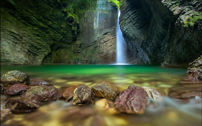 Waterfall cascading into a clear green pool surrounded by mossy rocks