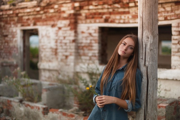 Young woman with flowers leaning against a wooden post