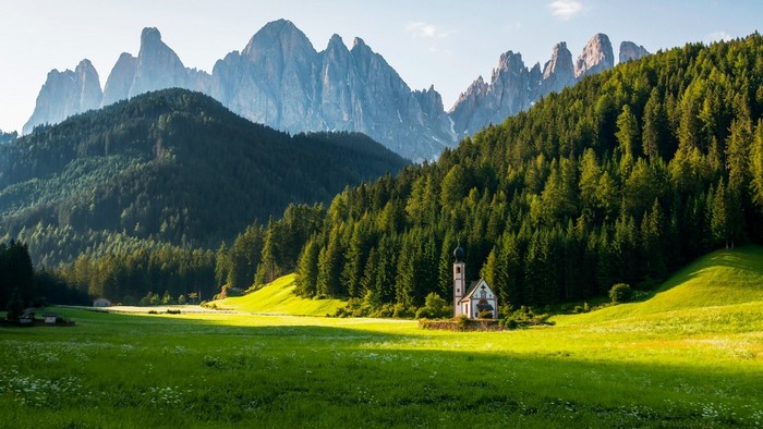 Chapel in a green valley with mountains and forest