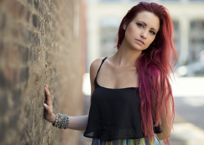Woman with dyed red hair leaning against a brick wall