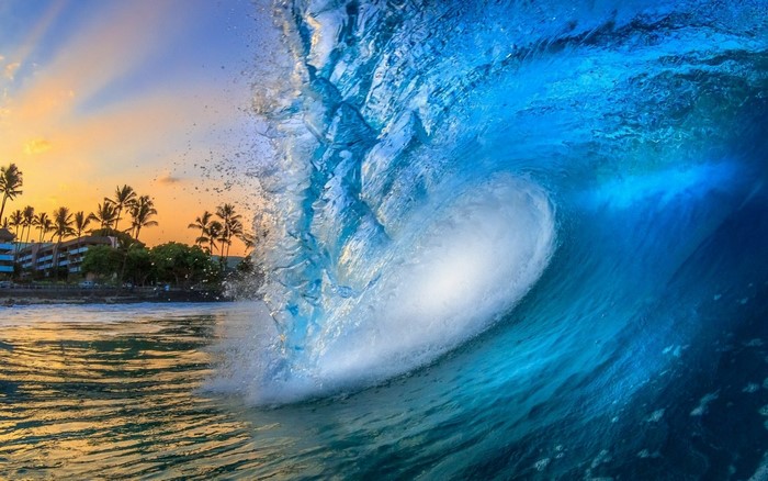 Ocean wave crashing at sunset with palm trees and buildings