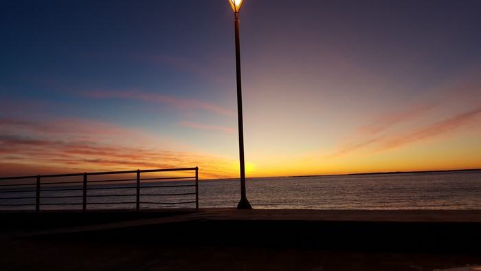 Sunset over the sea with a lamppost and railing