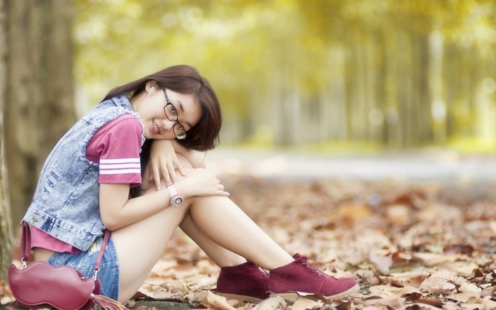 Young Asian woman with glasses sitting in autumn forest